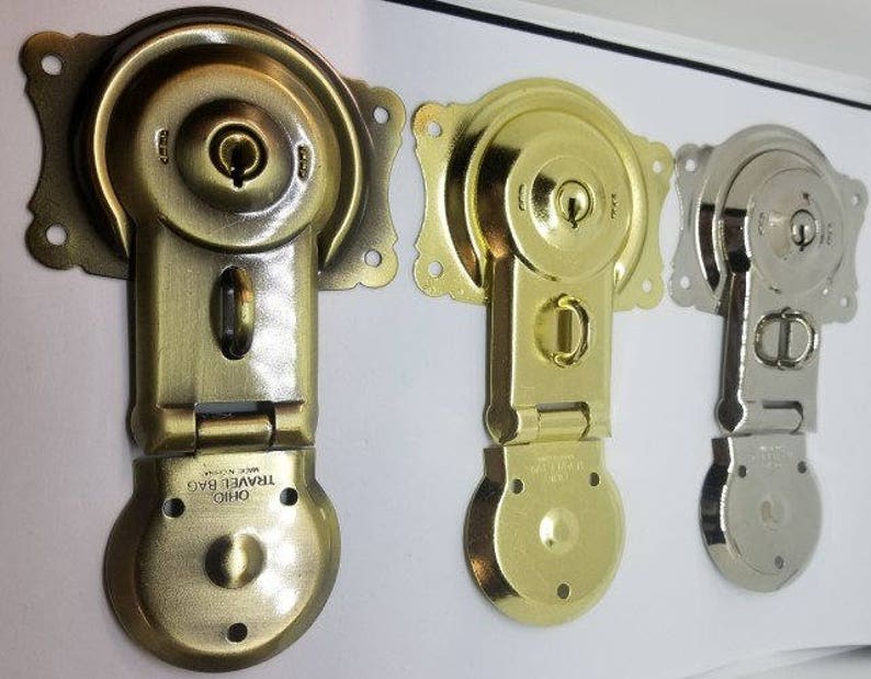 May include: Three antique-style metal clasps with keyholes and decorative details. The clasps are in gold, brass, and silver finishes. The clasps are labeled "Ohio Travel Bag Made in USA".