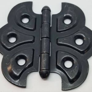 May include: Black metal butterfly hinge with a decorative design. The hinge has a traditional style and is made of durable metal.