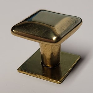 May include: A gold square cabinet knob with a raised square top and a square base.