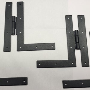 May include: Four black metal L-shaped hinges with a matte finish. The hinges are designed to be used for doors or gates that open at a 90-degree angle.