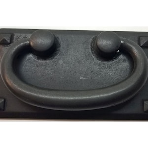 May include: Black metal drawer pull with a rounded rectangular base and a D-shaped handle. The pull has a distressed finish and four decorative studs on the base.