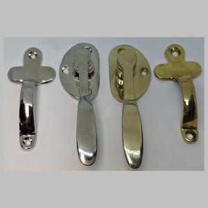 May include: Four metal window or cabinet latches in silver and gold tones. Two are silver, one with a cross-shaped handle and the other with an oval base. The other two are gold, with similar designs. These are likely vintage or antique hardware.