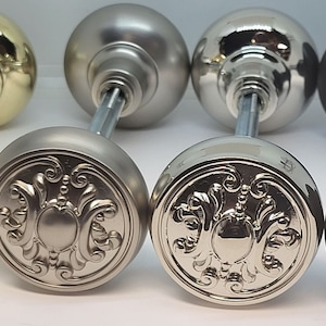 May include: Four door knobs in different finishes: brass, nickel, polished nickel, and oil rubbed bronze. Each knob features a decorative, ornate design.