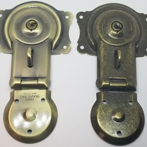 May include: Two antique-style brass latch clasps with a keyhole and a small loop. The clasps are closed and have a textured finish. The bottom clasp has the text "OHIO TRAVEL BAG MADE IN CHINA" on the bottom.