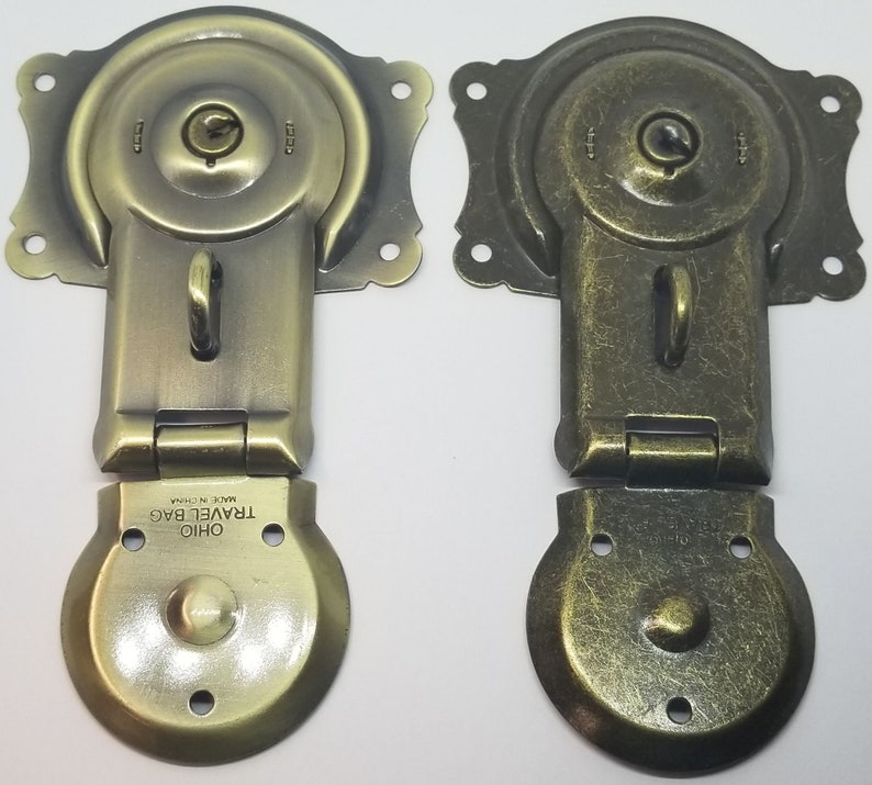 May include: Two antique-style brass latch clasps with a keyhole and a small loop. The clasps are closed and have a textured finish. The bottom clasp has the text "OHIO TRAVEL BAG MADE IN CHINA" on the bottom.