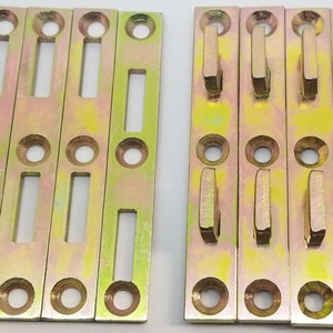 May include: Set of ten gold metal shelf brackets with a rectangular shape and two holes on each side. The brackets have a slot in the middle and a hook on one end.