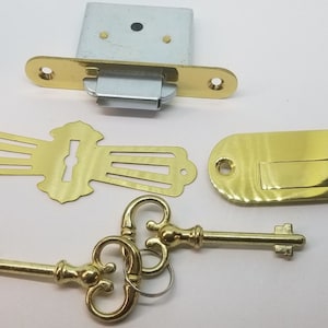 May include: A set of gold-toned door hardware, including a latch, strike plate, keyhole cover, and two keys. The keys have ornate designs.