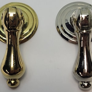 May include: Two cabinet pulls, one gold-toned and one silver-toned, are displayed against a white background. Each pull features a circular backplate and a teardrop-shaped handle. The gold pull has a shiny finish, while the silver pull has a polished appearance.