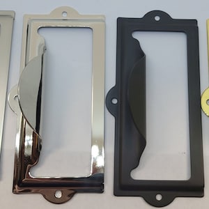 May include: Four metal label holders in different finishes: silver, chrome, black, and gold. Each holder has a curved top and a rectangular opening for a label.