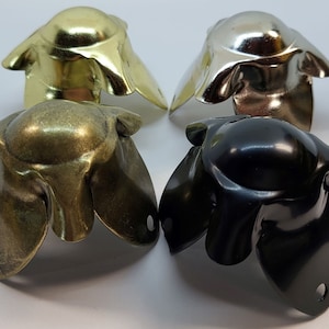 May include: Four metal furniture corner protectors in different finishes: gold, brass, silver, and black. Each protector has a flower-like design with five petals.