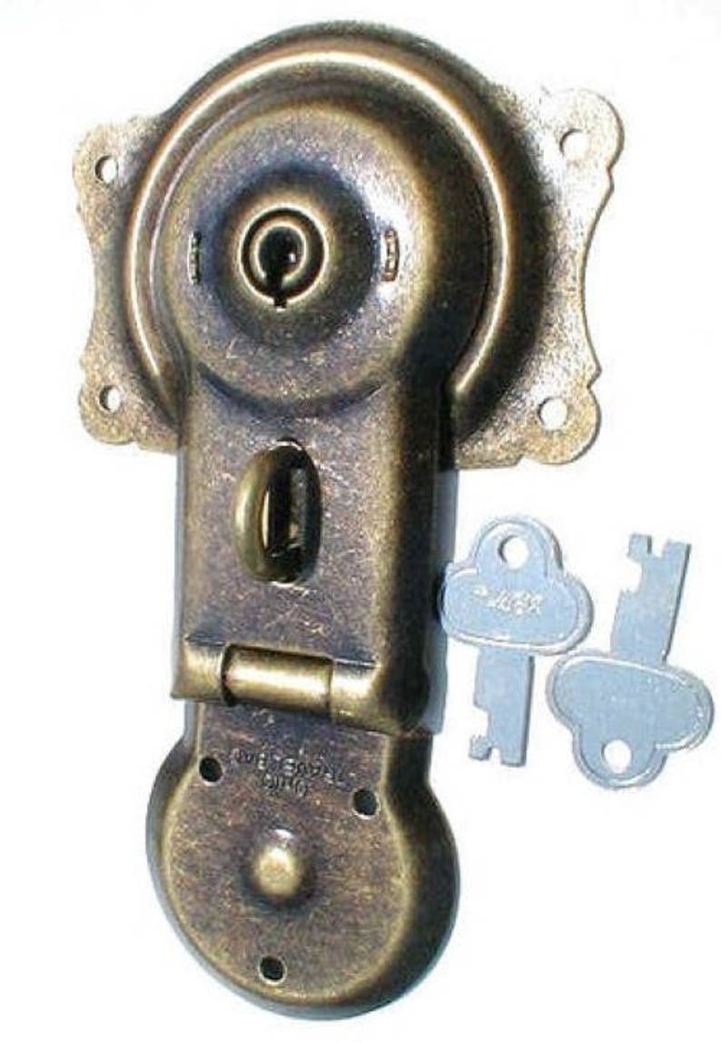 May include: Antique brass lock with a keyhole and two keys. The lock has a round shape and a hinged lid. The keys are silver and have a cloud-like shape.