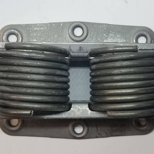 May include: A pair of silver metal springs attached to a metal plate with four holes. The springs are coiled and have a silver finish.