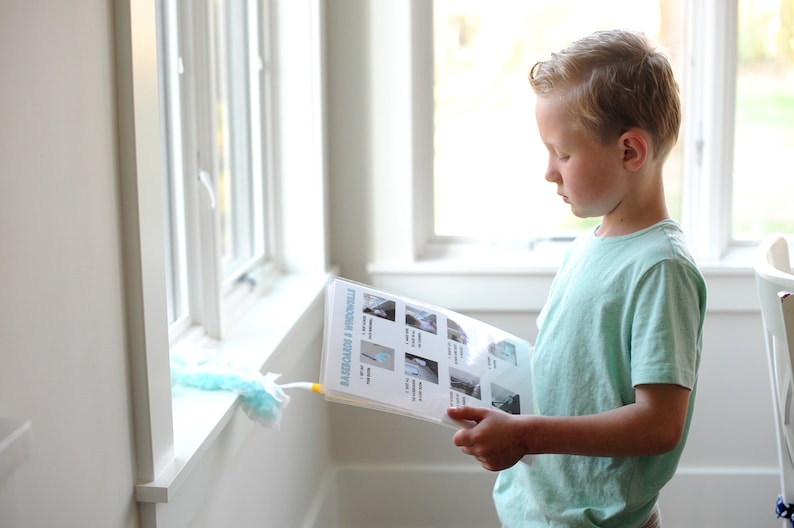 May include: A young boy is looking at a checklist titled "Mission Possible" with pictures of household chores. The checklist is on a white background with blue text and images.