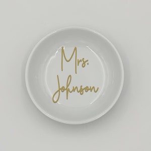 May include: White ceramic ring dish with the text "Mrs. Johnson" in gold lettering.