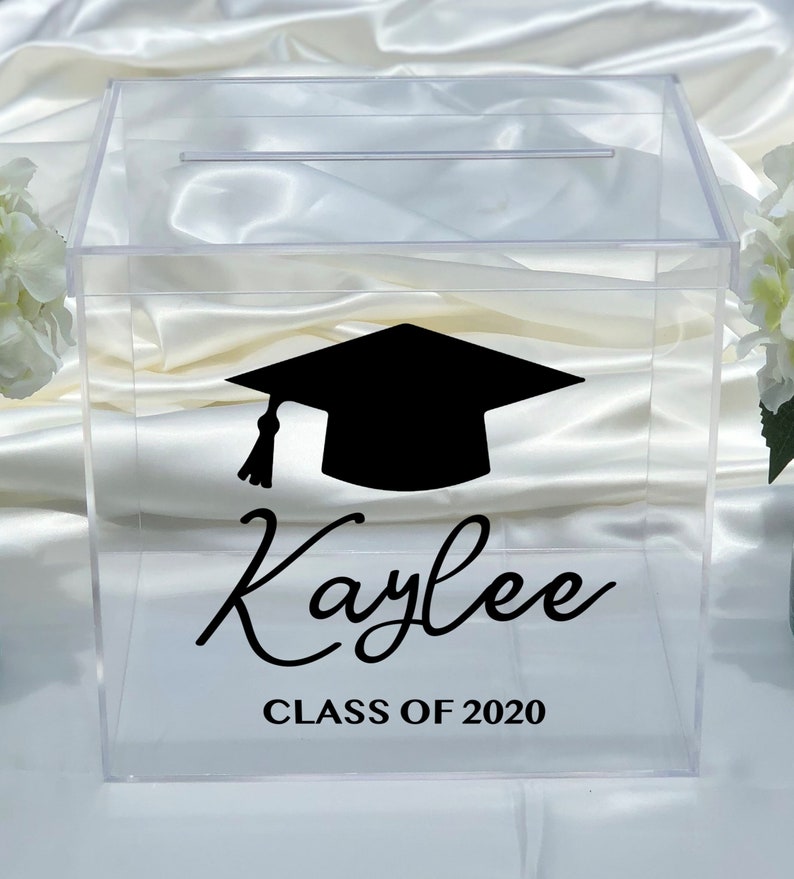 May include: Clear acrylic graduation box with a slot on top. A black graduation cap graphic and the name "Kaylee" are displayed in a stylish font. Below, the text "CLASS OF 2020" is printed in a simple font.