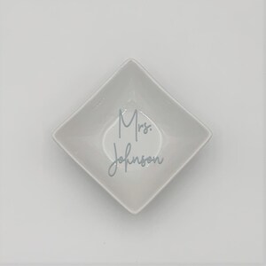May include: White ceramic square dish with the text "Mrs. Johnson" written in gray cursive.