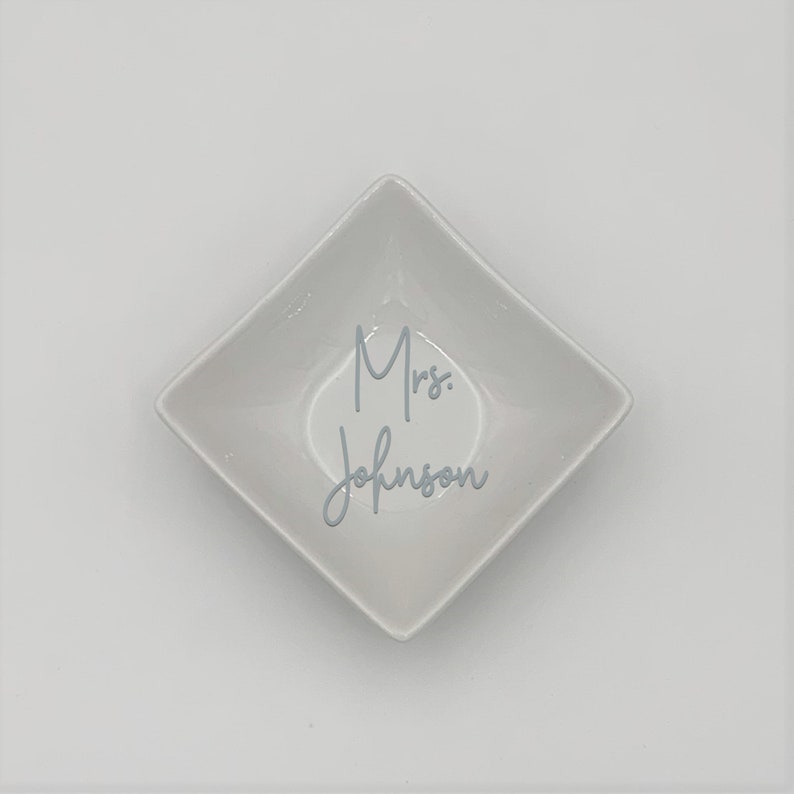 May include: White ceramic square dish with the text "Mrs. Johnson" written in gray cursive.