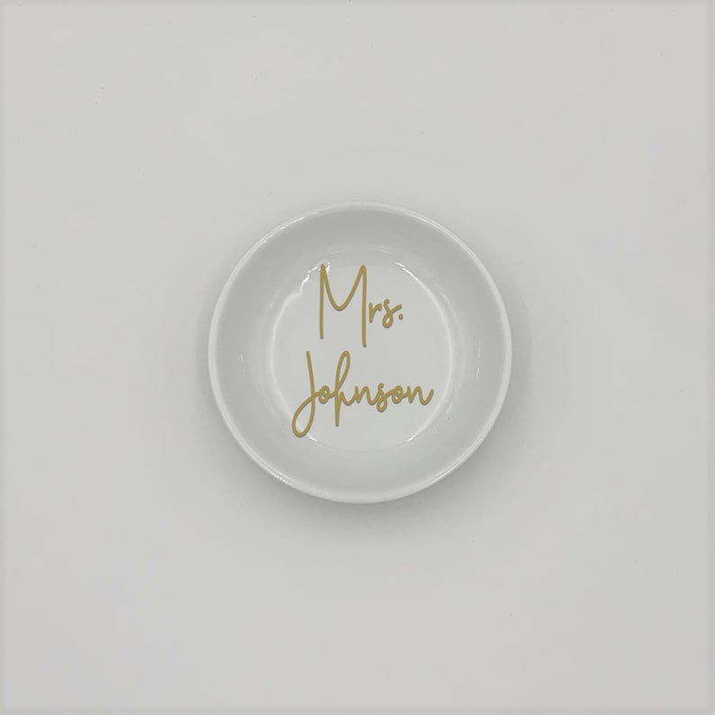 May include: White ceramic ring dish with the text "Mrs. Johnson" in gold lettering.