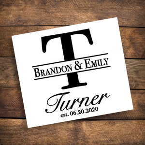 Pode incluir: Um sinal de casamento preto e branco com o sobrenome "Turner" e o texto "Brandon & Emily est. 06.20.2020". A primeira letra do sobrenome é um grande "T" maiúsculo com uma linha horizontal acima e abaixo.