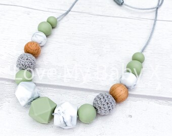 May include: A green, white, and brown silicone teething necklace with a gray cord. The necklace features various shapes and textures, including geometric, marble, and crocheted beads.