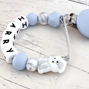 May include: A blue and white silicone baby teether with the name "HARRY" spelled out in white letters on the beads. The teether has a clip for attaching to clothing and a small white silicone dog charm.