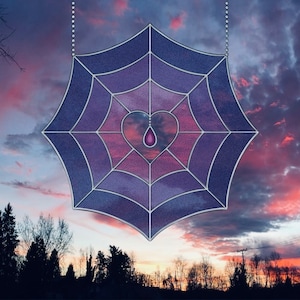 May include: A stained glass window hanging from a chain, shaped like a spider web with a purple and pink gradient. A heart shape is in the center of the web with a purple teardrop hanging from it.