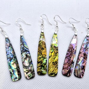 May include: A set of six long, iridescent abalone shell earrings with silver hooks. The earrings are a mix of green, blue, purple, and gold colours.