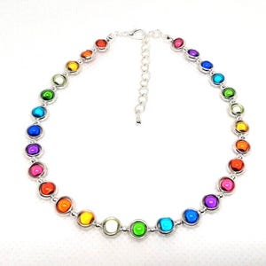 May include: A silver necklace with a series of colourful, round gemstones. The gemstones are arranged in a rainbow spectrum, with colours including red, orange, yellow, green, blue, and purple. The necklace has an adjustable chain.