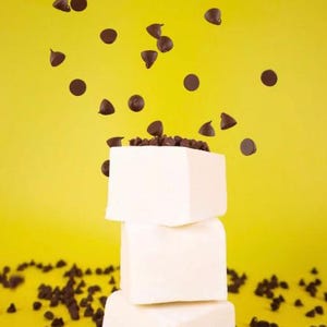 Puede incluir: Una pila de tres malvaviscos blancos con chispas de chocolate esparcidas alrededor y cayendo sobre los malvaviscos.