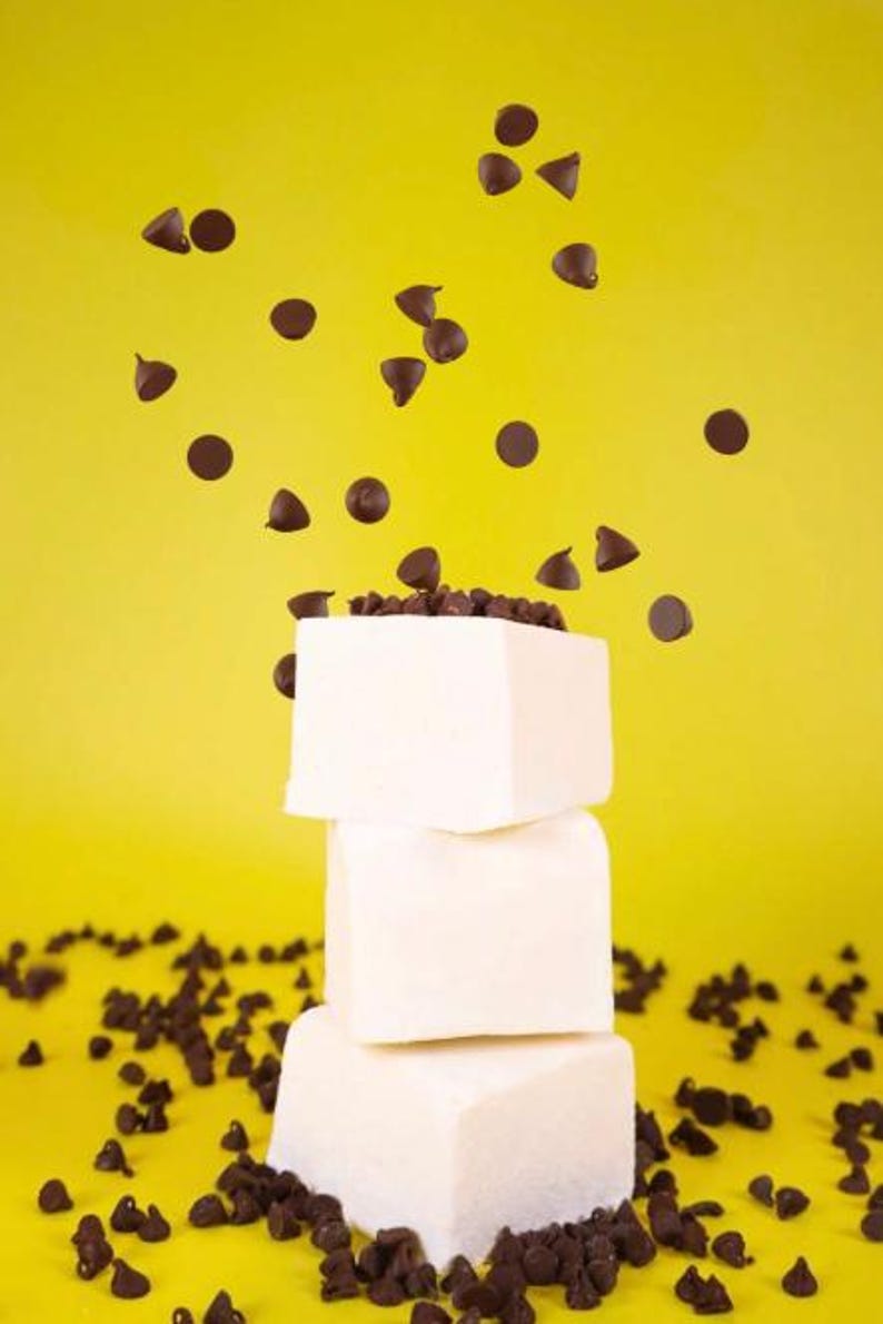 Puede incluir: Una pila de tres malvaviscos blancos con chispas de chocolate esparcidas alrededor y cayendo sobre los malvaviscos.