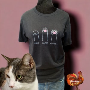 May include: A dark gray t-shirt with a white graphic of three cat paws. The paws are labeled "rock", "paper", and "scissors".