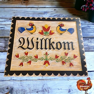May include: A wooden sign with a scalloped black border and a cream background. The sign features two stylized birds with blue and yellow feathers, red flowers, and green leaves. The word "Willkommen" is written in black lettering.
