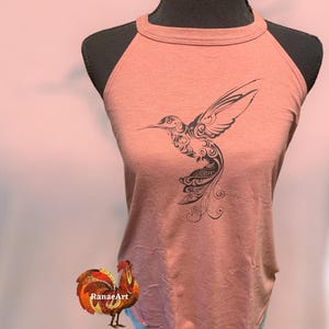 May include: A salmon-colored tank top with a black hummingbird design. The hummingbird is stylized with intricate details and has a long, curved beak.