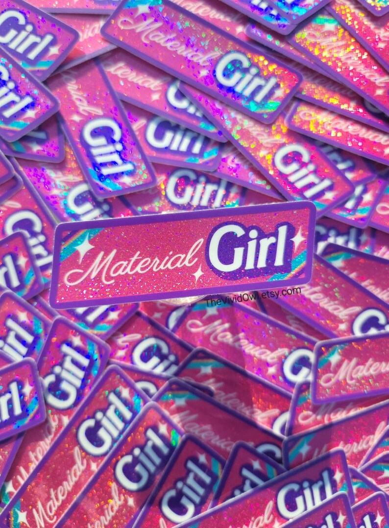 May include: A pile of pink and purple stickers with the words "Material Girl" and "Girl" in white script. The stickers have a glittery, holographic effect and a rectangular shape. The Etsy shop name is visible.