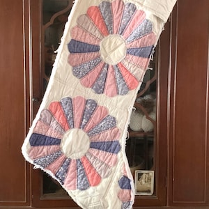 May include: A vintage quilted Christmas stocking with a pink and blue floral design. The stocking is hanging on a wooden cabinet with a glass door.