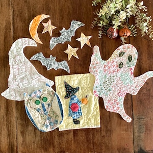 May include: A collection of quilted fabric Halloween decorations including a white witch hat, a ghost with a floral pattern, an owl, a rectangular piece with a witch figure, two grey bats, an orange crescent moon, and three small stars.