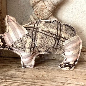 May include: A brown and white patchwork pig toy with a striped pattern. The pig is made of fabric and has a stitched snout and ears.