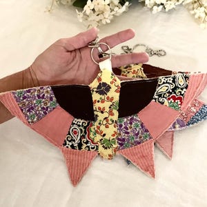 May include: A handmade butterfly-shaped keychain with a patchwork design. The wings feature various patterned fabrics in pink, purple, and floral prints. The center is yellow with a floral pattern. A silver keyring is attached.