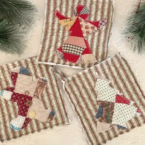 May include: Three quilted pot holders with a Christmas theme. The pot holders are made of a green and white striped fabric with a patchwork design. One pot holder features a red and white angel, another features a red and white teddy bear, and the third features a green and white Christmas tree.