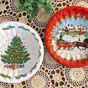 May include: Two vintage Christmas themed metal serving dishes. One dish is white with a green Christmas tree and red and white ornaments. The other dish is red with a winter scene of a house, a horse-drawn carriage, and a Christmas tree.