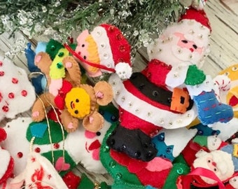 May include: A collection of vintage felt Christmas ornaments featuring Santa Claus, a snowman, a reindeer, and other festive characters. The ornaments are decorated with sequins and beads.