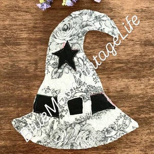 May include: A decorative witch hat with a floral pattern in black and white. The hat features a black star and buckle details. The text "Blue Moon Vintage Life" is visible on the hat.