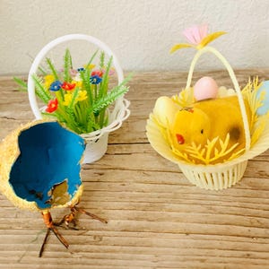 May include: Three vintage Easter baskets, one with a yellow chick and two eggs, one with a bouquet of colorful flowers, and one with a blue and brown egg with wire legs.