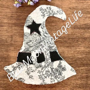 May include: A decorative witch hat with a black star and black band. The hat is white with a floral pattern in black and gray. The text "Blue Moon Vintage Life" is on the hat.