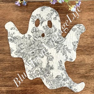 May include: A white ghost-shaped decoration with a floral pattern in shades of gray. The ghost has two eye holes and a mouth hole. The words "Blue Vintage Life" are written on the ghost.