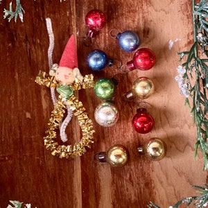 May include: A collection of vintage glass ornaments in various colors, including red, blue, green, gold, and silver. A small handmade doll with a red hat and gold tinsel is also included.