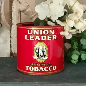 May include: Red metal tin with a white label that reads "UNION LEADER SMOKING TOBACCO". The label also features a gold eagle with a red, white, and blue ribbon.