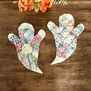 May include: Two ghost-shaped fabric ornaments crafted from quilted patchwork fabric. Each ghost features a variety of colorful patterns including plaid, gingham, and floral prints in shades of red, blue, green, and white, with a white fabric base.