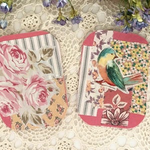 May include: Two handmade fabric tags with pink edges. One features pink roses on a floral background, the other a colorful bird on a branch. Both tags have a patchwork design with various floral patterns.
