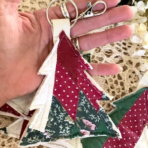 May include: A Christmas tree-shaped keychain with a silver clasp and key ring. The tree is made of fabric pieces in red with white polka dots, white, and green floral patterns. A white ribbon connects the tree to the hardware.